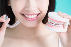 a woman holding Invisalign braces and a mold of traditional braces