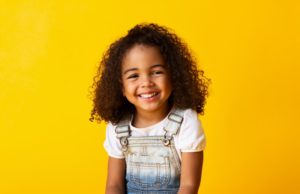 a little girl wearing overalls and smiling